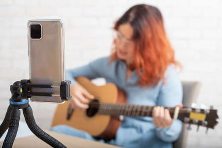 A woman is broadcasting online on her phone at home. The girl sings and plays the guitar liveの写真素材