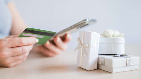 A faceless woman sits at a table and holds a mobile and a credit card in her hands. Online shopping for gifts conceptの写真素材