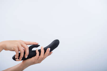 Faceless woman holding black dildo with clitoris stimulator on white backgroundの写真素材