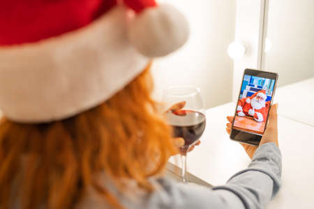 Woman makes a video call to santa claus and drinks red wine at christmas timeの写真素材