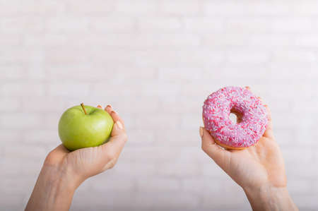 Donut and green apple in female hands. The concept of different eating habits. Thinness and obesity