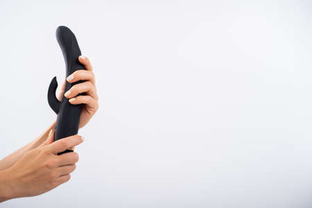 Faceless woman holding black dildo with clitoris stimulator on white background