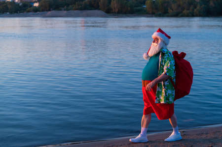 Santa Claus walks along the beach in shorts and a shirt. Christmas in a hot country