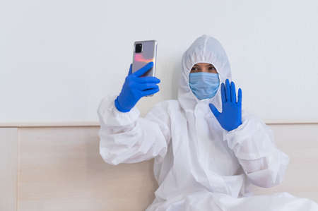 A female doctor in a protective suit makes a video call on a smartphoneの写真素材