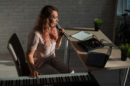 Expressive female singer has a video blog on a laptop. Portrait of a girl recording a song on a web...