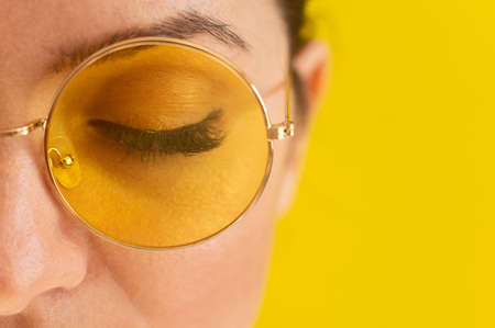 Close-up portrait of a woman in sunglasses on a yellow backgroundの写真素材