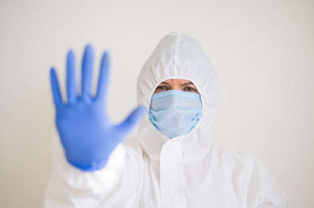 Woman in protective suit, medical mask and latex gloves, shows stop gesture. Tired doctor in the coronavirus epidemicの写真素材