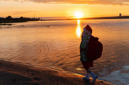Santa claus in shorts and a shirt walks along the beach at sunset. Christmas in a hot countryの写真素材