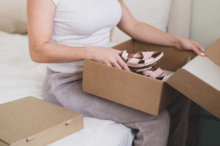 Happy woman unpacks online shopping for shoes. The girl received the package and opens it while sitting in the bedroomの写真素材