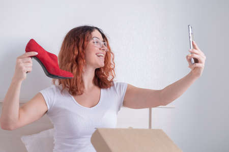 Caucasian woman sitting in bed and taking a selfie with a delivered purchase. Online shopping for shoesの写真素材