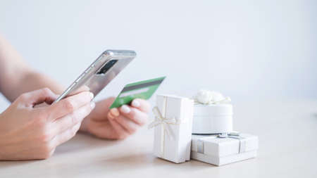 A faceless woman sits at a table and holds a mobile and a credit card in her hands. Online shopping...