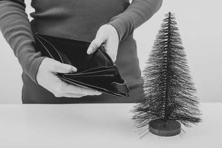 A woman is holding an empty purse next to a small artificial Christmas tree. The financial crisis...