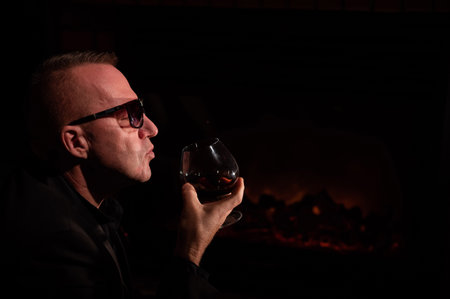 Mature man drinking cognac by the fireplace.の写真素材