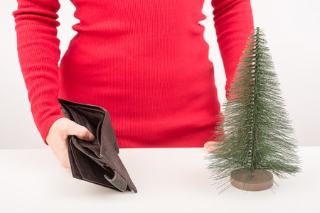 A woman is holding an empty purse next to a small artificial Christmas tree. The financial crisis...