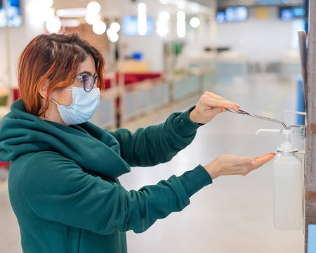 A woman uses a wall sanitizer in a public place. Close-up of female hands treating with antisepticの写真素材