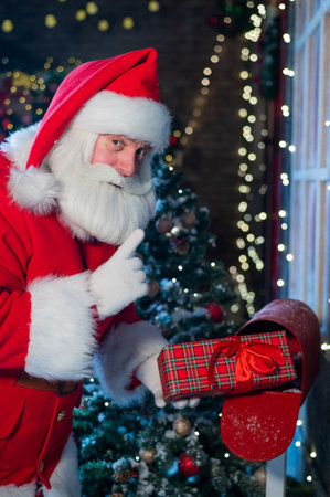 Santa Claus sends a gift by mail. A man dressed as a Santa puts a decorated box in a mailboxの写真素材
