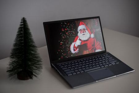 Santa Claus wishes Merry Christmas by video call on a laptop. Remote communicationの写真素材