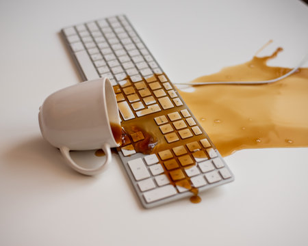 Spilled black coffee on a computer keyboard at a white tableの写真素材
