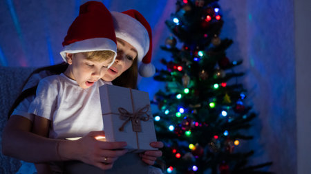 Exciting Mom and son open a glowing gift box at a magical Christmas nightの写真素材