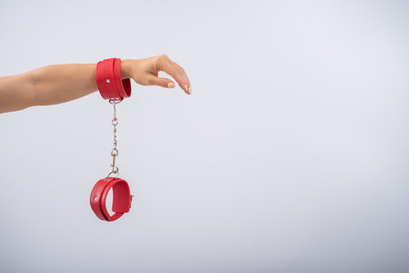 Red leather handcuffs in female hands on a white background. BDSM accessoriesの写真素材