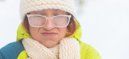 Portrait of a woman in glasses covered with hoarfrost. Upset girl freezing in very cold weather outdoors. Widescreen.の写真素材