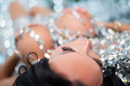 Sexy nude brunette woman with a large seductive breast lies among the silvery sequinsの写真素材