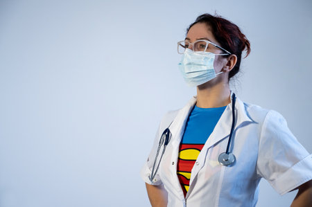 12.07.2020 Russia, Novosibirsk: Female doctor wearing a medical mask unbuttons his coat and exposes a superman suit.のeditorial素材