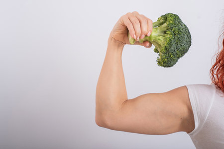 Muscular woman holding broccoli. Female biceps