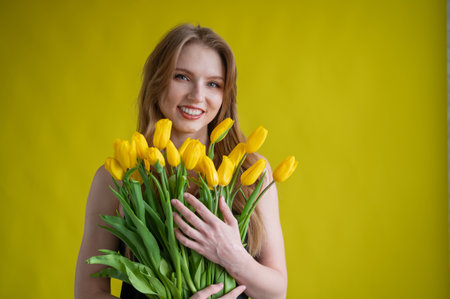 Caucasian woman with an armful of yellow tulips on a yellow background. International Womens Day. Bouquet of spring flowersの写真素材
