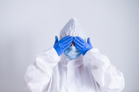 A woman in a protective suit and a medical mask covers her eyes with her hands. I do not see evilの写真素材