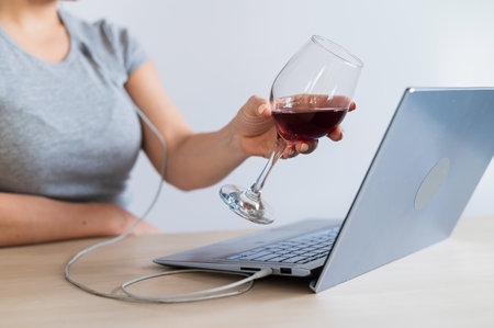 Caucasian woman toasting with a glass of red wine during a video call at home. Remote communication in isolationの写真素材