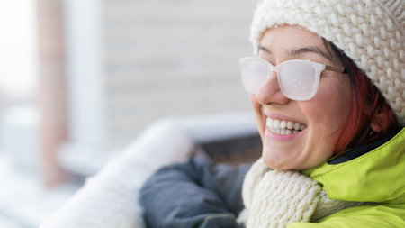 Smiling Caucasian woman stands on the balcony of a brick house in winter. Happy girl in ice-covered...