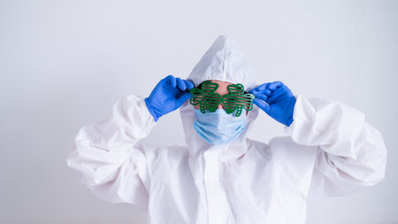 A woman in a protective suit and a medical mask and wearing funny glasses celebrates st patricks dayの写真素材