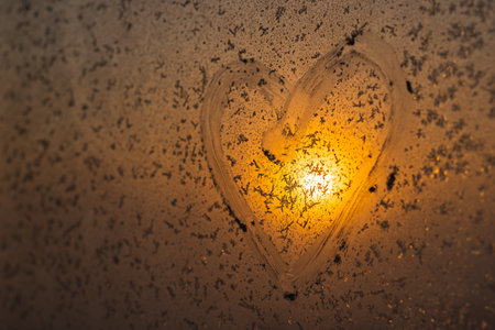 A heart drawn on a frozen winter window at sunset.の写真素材