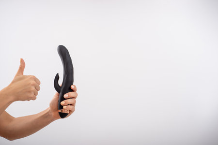 Faceless woman holding black dildo with clitoris stimulator on white backgroundの写真素材
