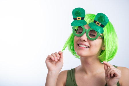 Cheerful young woman in green wig and funny glasses celebrating st patricks day on a white background. Copy spaceの写真素材