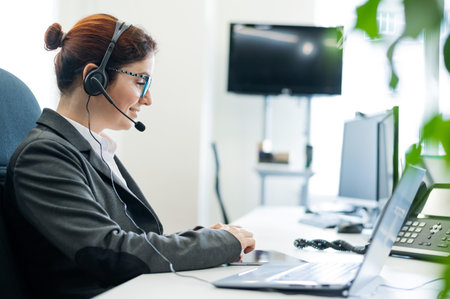 Woman in headset sits at her desk in the office and uses digital tabletの写真素材