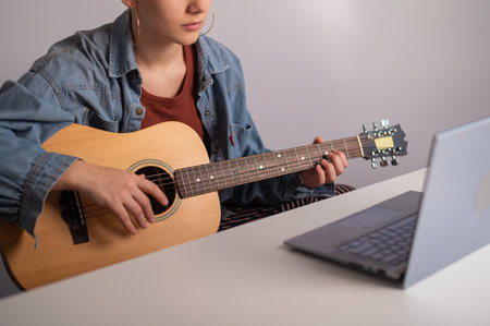Young woman is learning to play the guitar online. Remote music lessons on a laptopの写真素材
