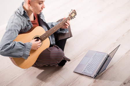 Young hipster woman watching guitar tutorials on laptop. Distance learning music