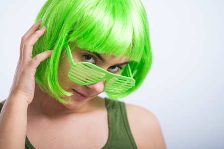 Cheerful young woman in green wig and funny glasses celebrating st patricks day on a white backgroundの写真素材