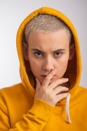 Young woman in ocher hood covers her face with hand on white background.の写真素材