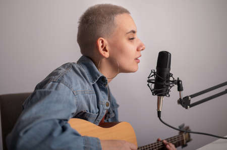 Close-up portrait of young woman playing guitar and singing into microphone on white background.