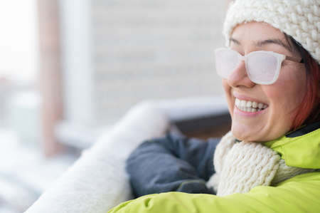 Smiling Caucasian woman stands on the balcony of a brick house in winter. Happy girl in ice-covered...
