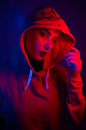 Portrait of a beautiful young woman in a sweatshirt with a hood in neon lightの写真素材