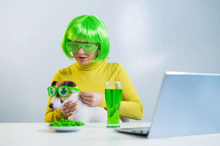 A young woman in a green wig and cheerful glasses drinks beer and bites glazed nuts. A girl sits...