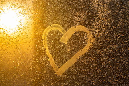 A heart drawn on a frozen winter window at sunset.の写真素材