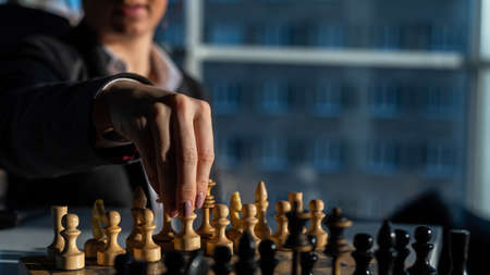 Business woman in a suit plays chess. Close-up of a female hand on a pawnの写真素材