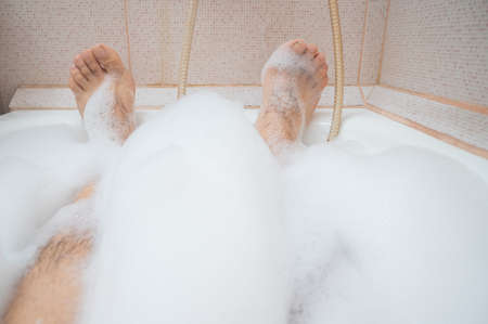 Close-up of male hairy legs in foam. A faceless man is taking a relaxing bathの写真素材