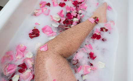 Funny picture of a man taking a relaxing bath. Close-up of male feet in a bath with foam and rose...