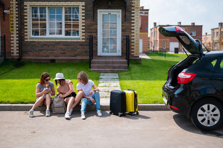 Three Caucasian women and a dog are going on a road trip. The girls are loading their suitcases into the trunk of the car. Summer vacation concept together with girlfriends.の写真素材
